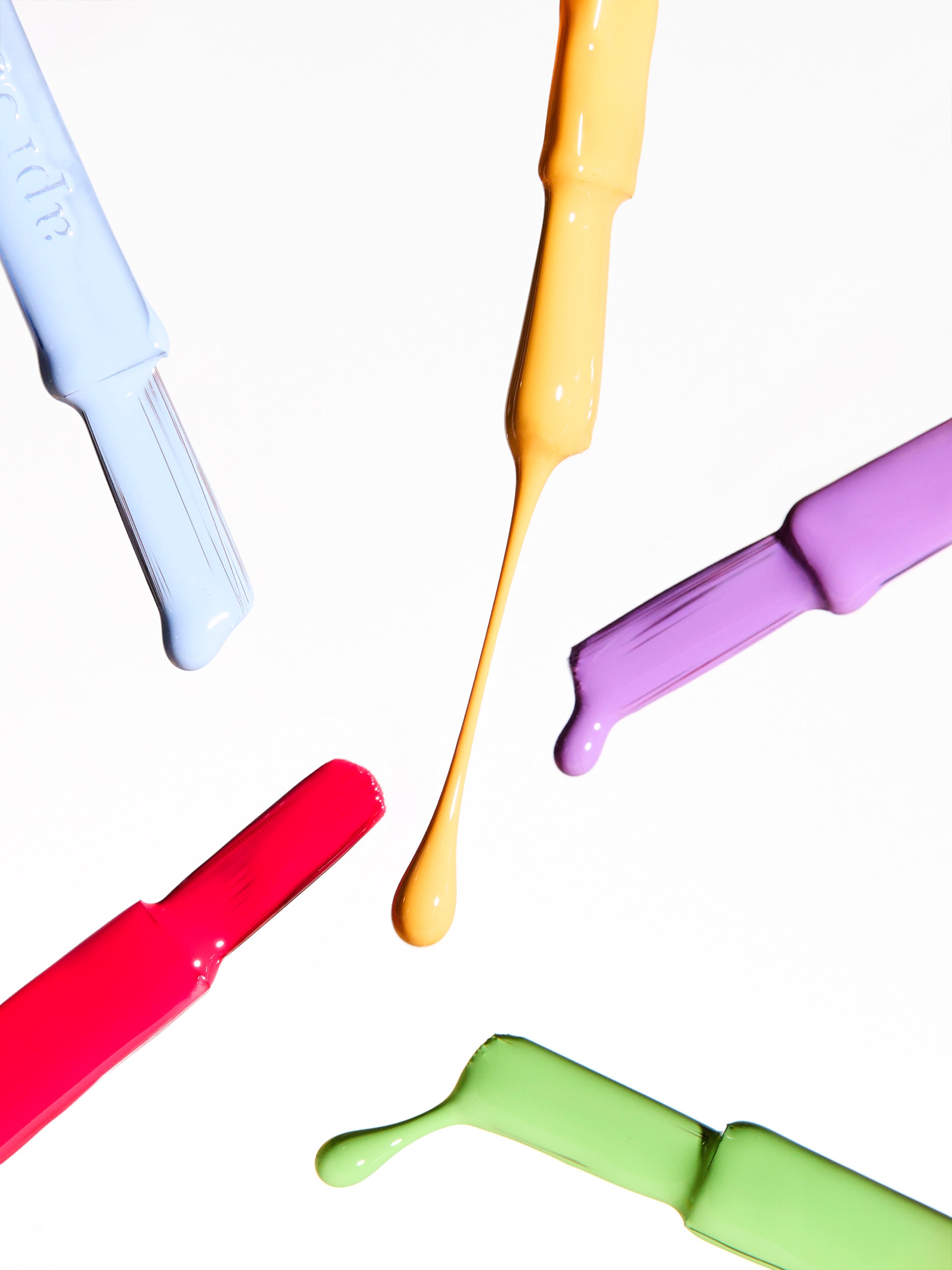 Colorful nail applicators with liquid droplets on a white background