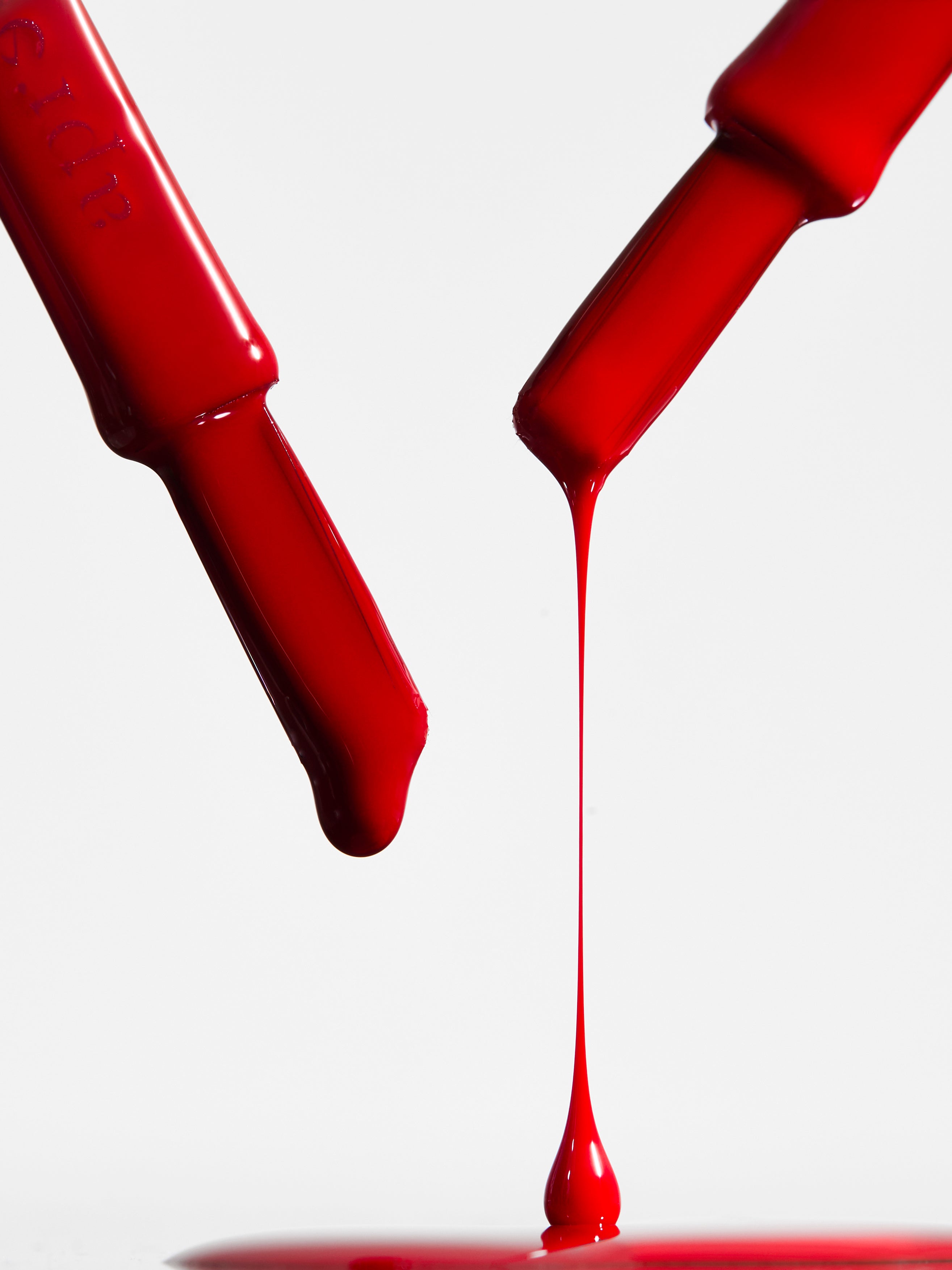 Red nail polish bottle with a droplet of red liquid on a white background
