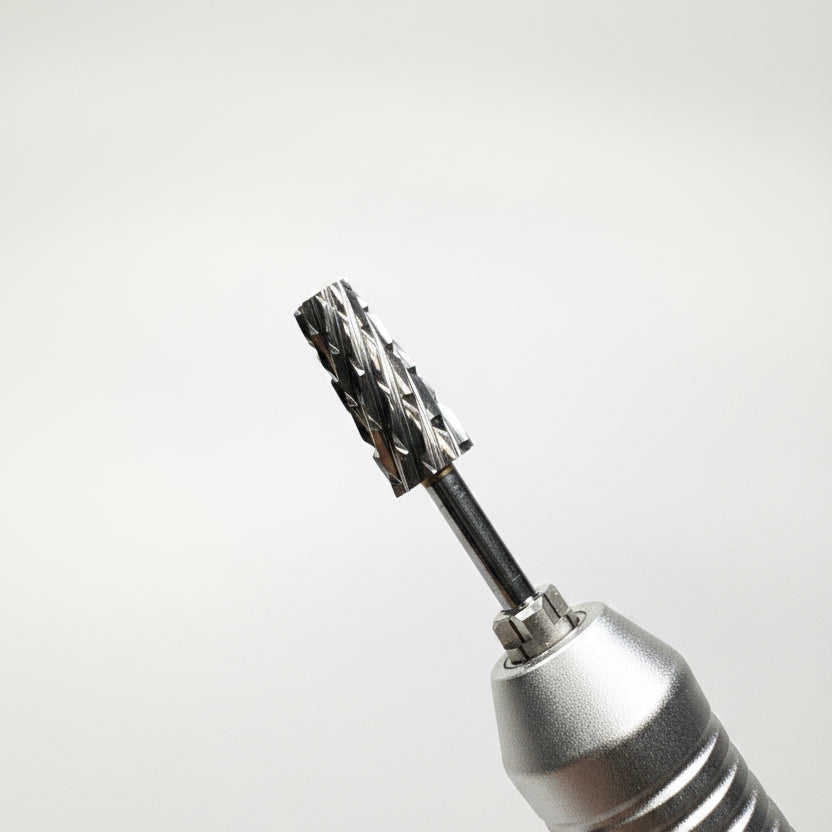 A close-up of a rotary dental drill bit attachment with a textured silver metal handle and a black drill bit, shown against a soft gray gradient background.