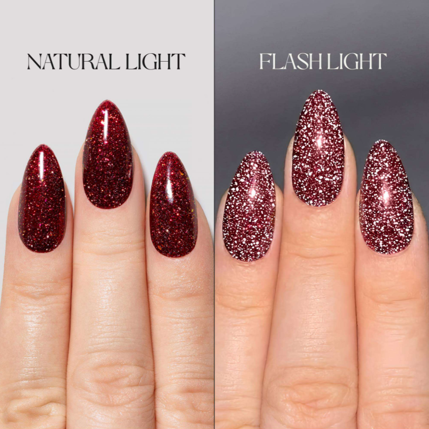A split-screen comparison showing glittery red press-on nails on a person's fingers under natural light and flash light. The left side is labeled 'NATURAL LIGHT' and shows a deep red glitter finish.