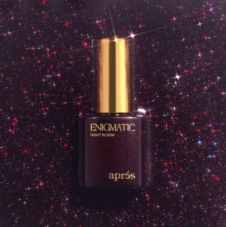 A bottle of aprés Enigmatic Night Bloom nail polish, featuring a dark, shimmering plum-brown color with a metallic gold cap, set against a sparkling starry background.