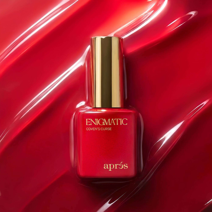 Apres Enigmatic Cover's Curse nail polish bottle in a glossy red shade with a gold cap, set against a matching red background with a liquid wave texture.