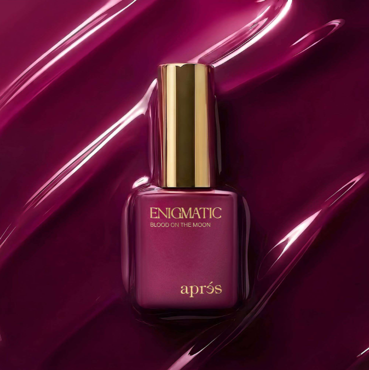 Apres Enigmatic Blush on the Moon nail polish bottle, featuring a deep magenta-purple color with a shiny gold cap, set against a matching glossy purple background.