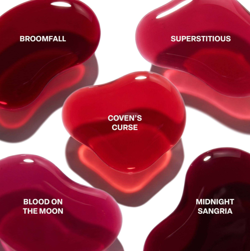 Five glossy red translucent jelly beans arranged on a white background, each labeled with a scent name: Broomfall, Superstitious, Coven's Curse, Blood on the Moon, and Midnight Sangria.