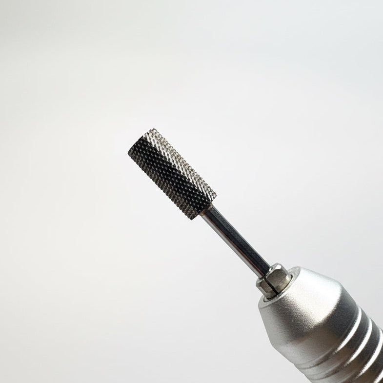 Close-up of a silver handheld rotary tool with a black textured metal burr bit, shown against a soft gray gradient background.