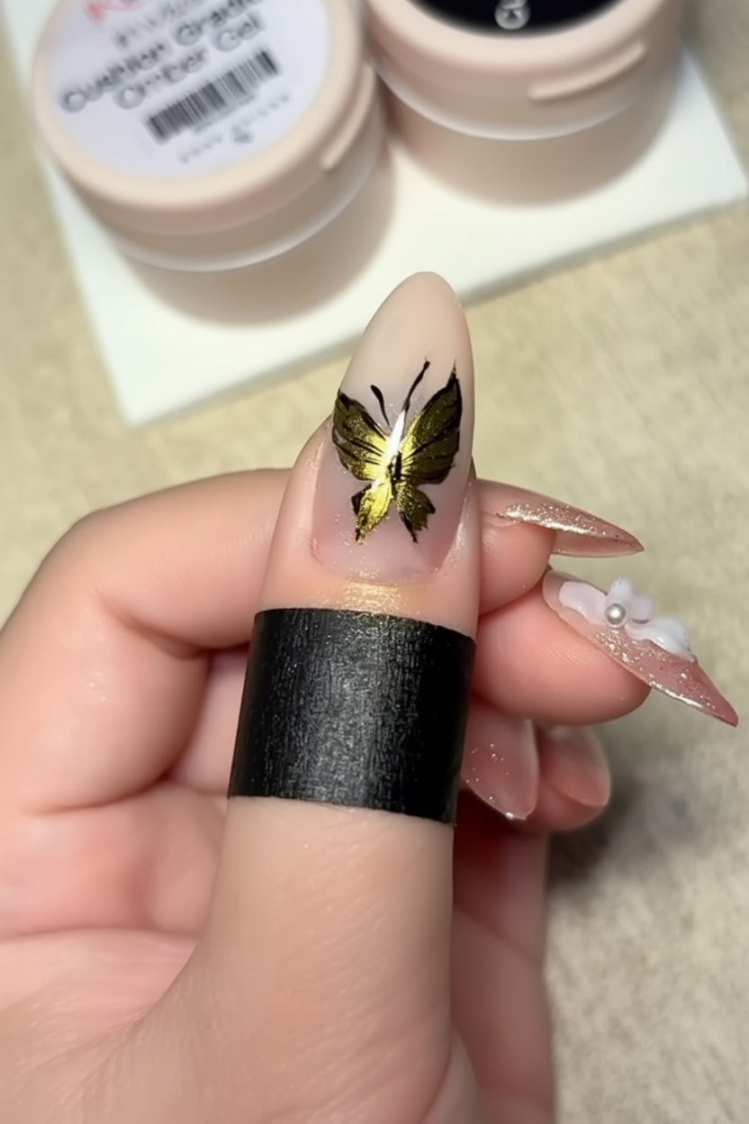 Nail with gold butterfly design held by a hand, with a blurred background