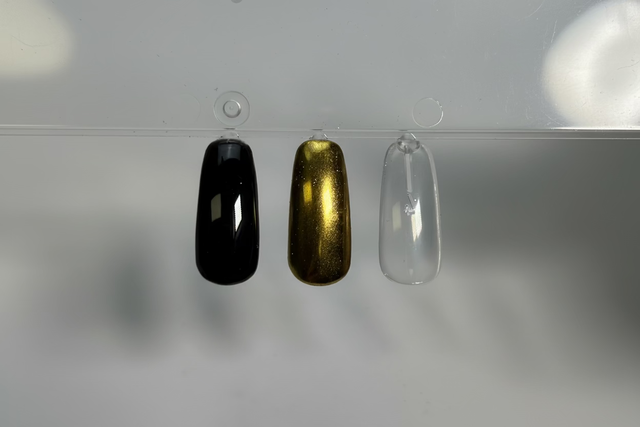 Three nail polish samples in black, gold, and clear on a gray background