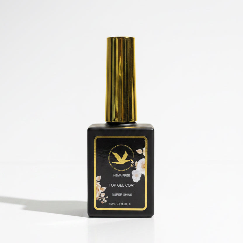 A bottle of HEMATREE Hemat-free Top Gel Coat Super Shine nail polish top, featuring a black rectangular bottle with a shiny gold cap and a black label with gold and white floral accents, set on a wooden surface against a neutral gray background.