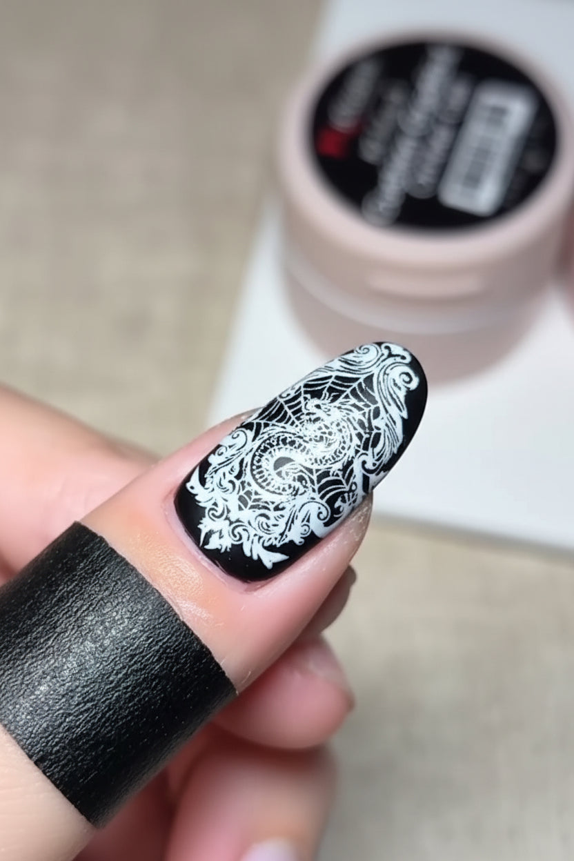 Nail with black and white floral design held by a hand, with a nail polish bottle in the background.