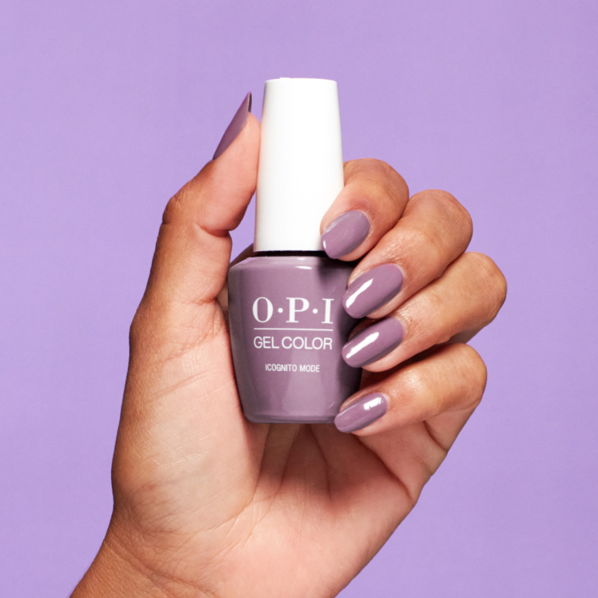 Hand holding an OPI nail polish bottle with a matching purple nail color against a purple background