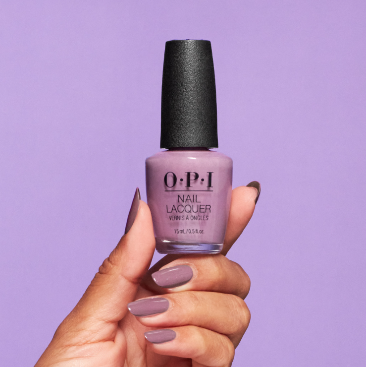 Hand holding a bottle of OPI nail polish with a purple background
