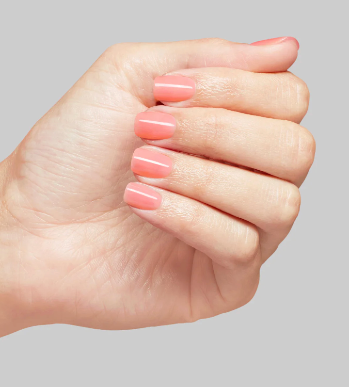 Hand with pink nail polish on a gray background