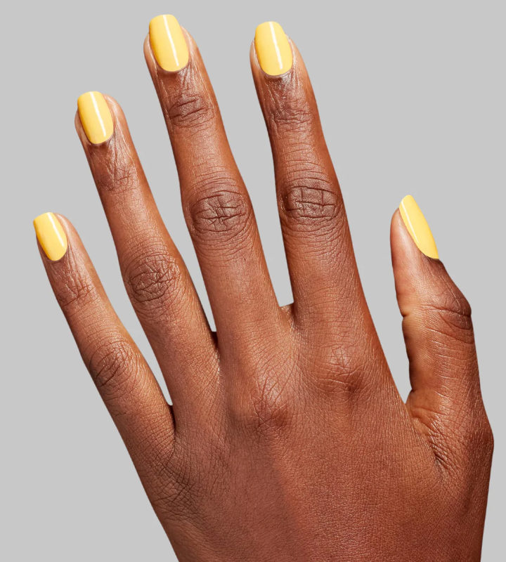 Hand with yellow nail polish on a gray background