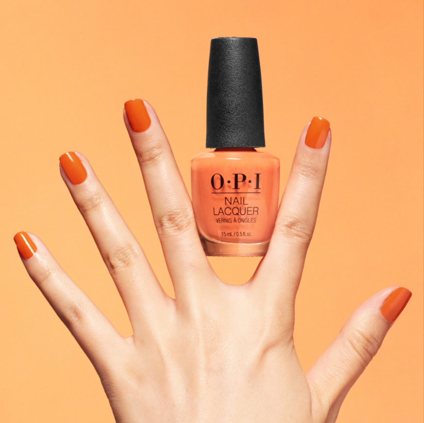 OPI nail polish bottle held by a hand with orange nails against an orange background