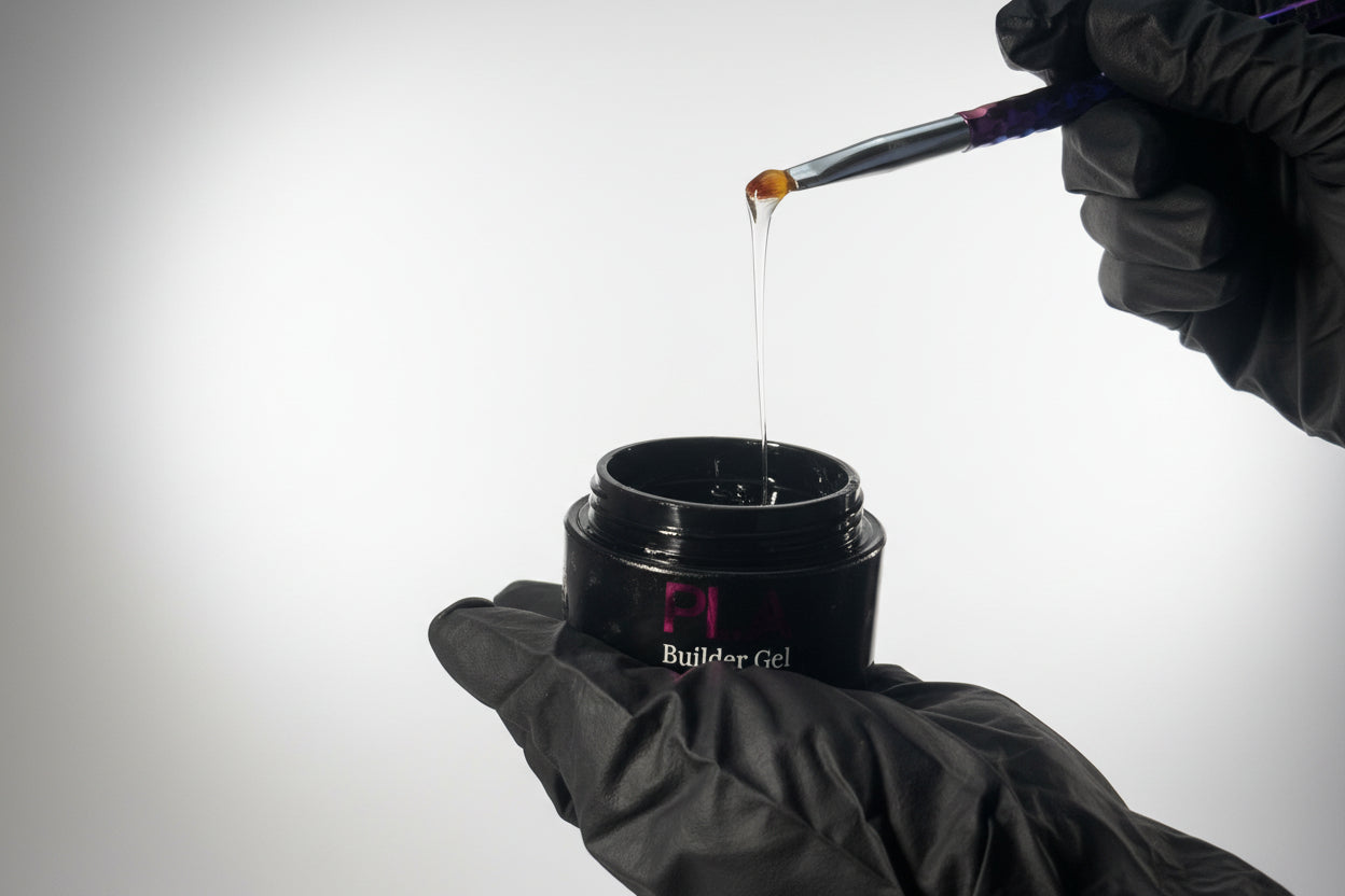 Person applying gel to a brush from a container labeled 'Builder Gel' on a neutral background.