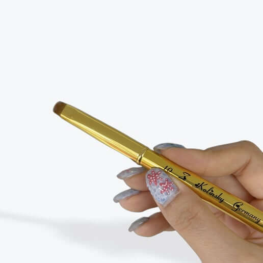 Gold pen held by a hand with decorative nails on a white background
