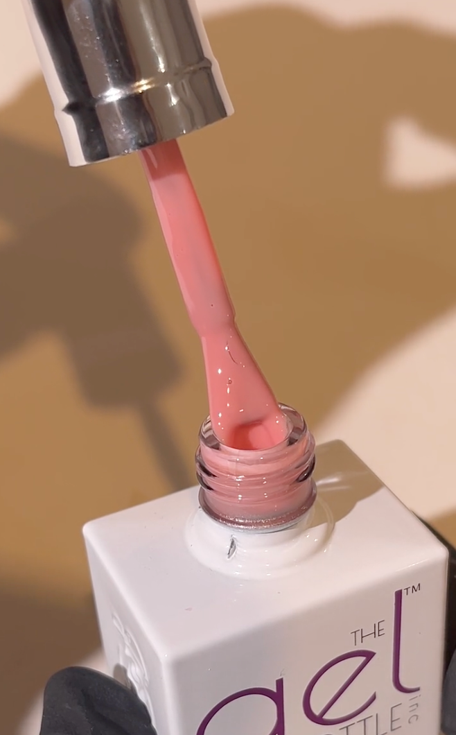 Pink nail polish being applied with a brush, against a beige background.