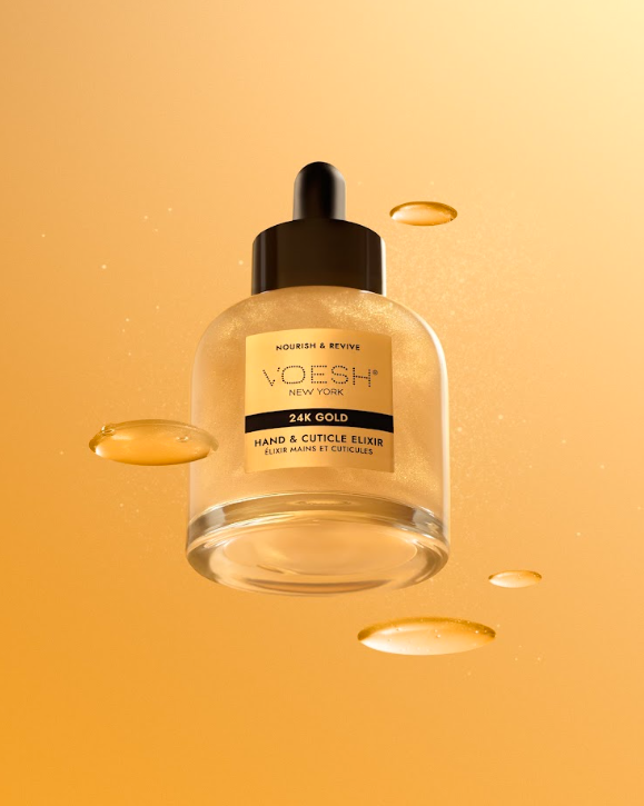 A glass dropper bottle of Voesh New York 24K Gold Hand & Cuticle Elixir floating against a warm golden-orange background with decorative liquid droplets.