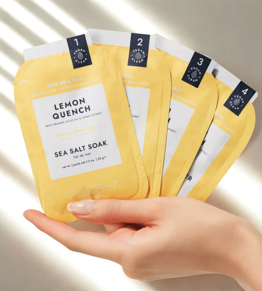 Hand holding a package of Lemon Quench sea salt soaks with a neutral background