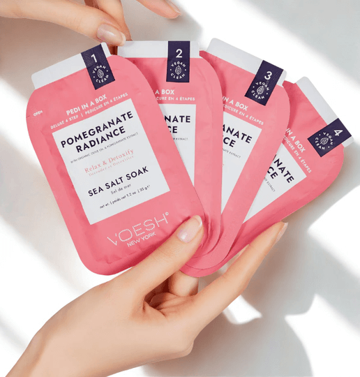 Pink 'Pomegranate Radiance' sea salt soaks with Voesh branding held by a hand on a light background.
